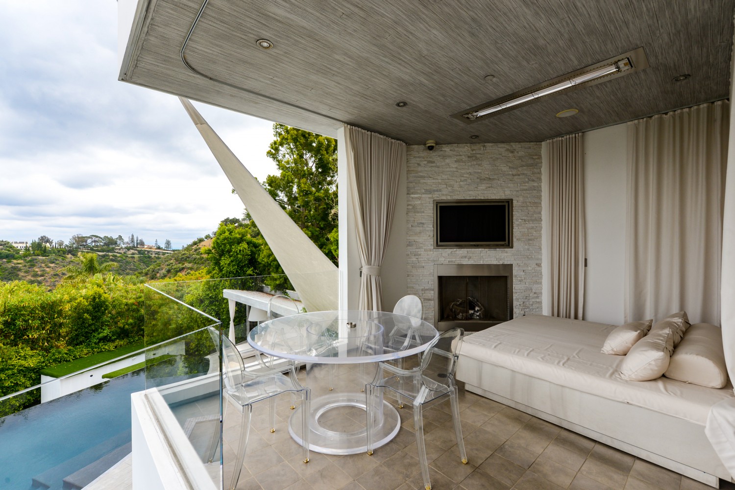 Resort-style outdoor cabana featuring a fireplace, lounge seating, and panoramic canyon views at a modern Bel Air estate.
