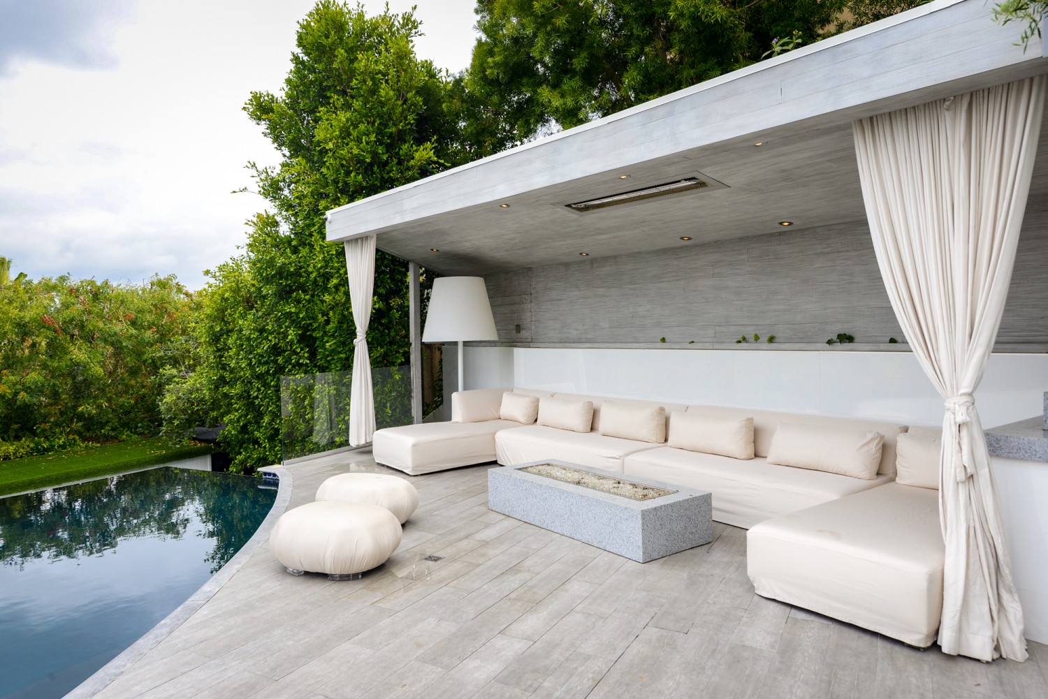 Covered outdoor lounge beside the infinity-edge pool with comfortable seating and contemporary design in Bel Air.