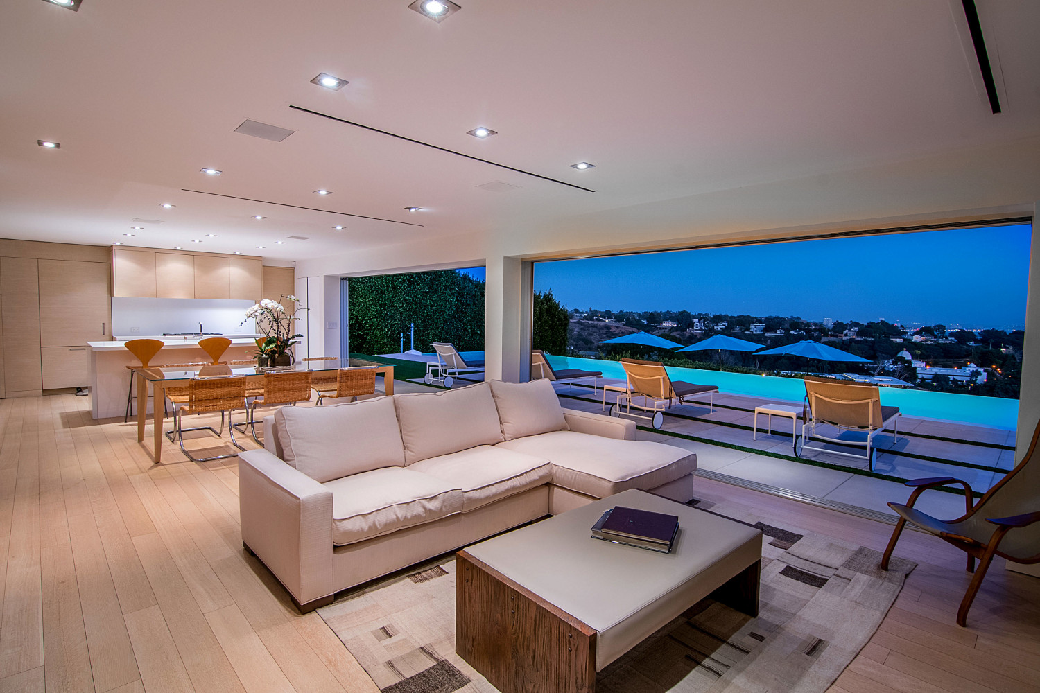 Great room featuring expansive retractable glass walls, contemporary furnishings, and sweeping Pacific Ocean views at dusk.