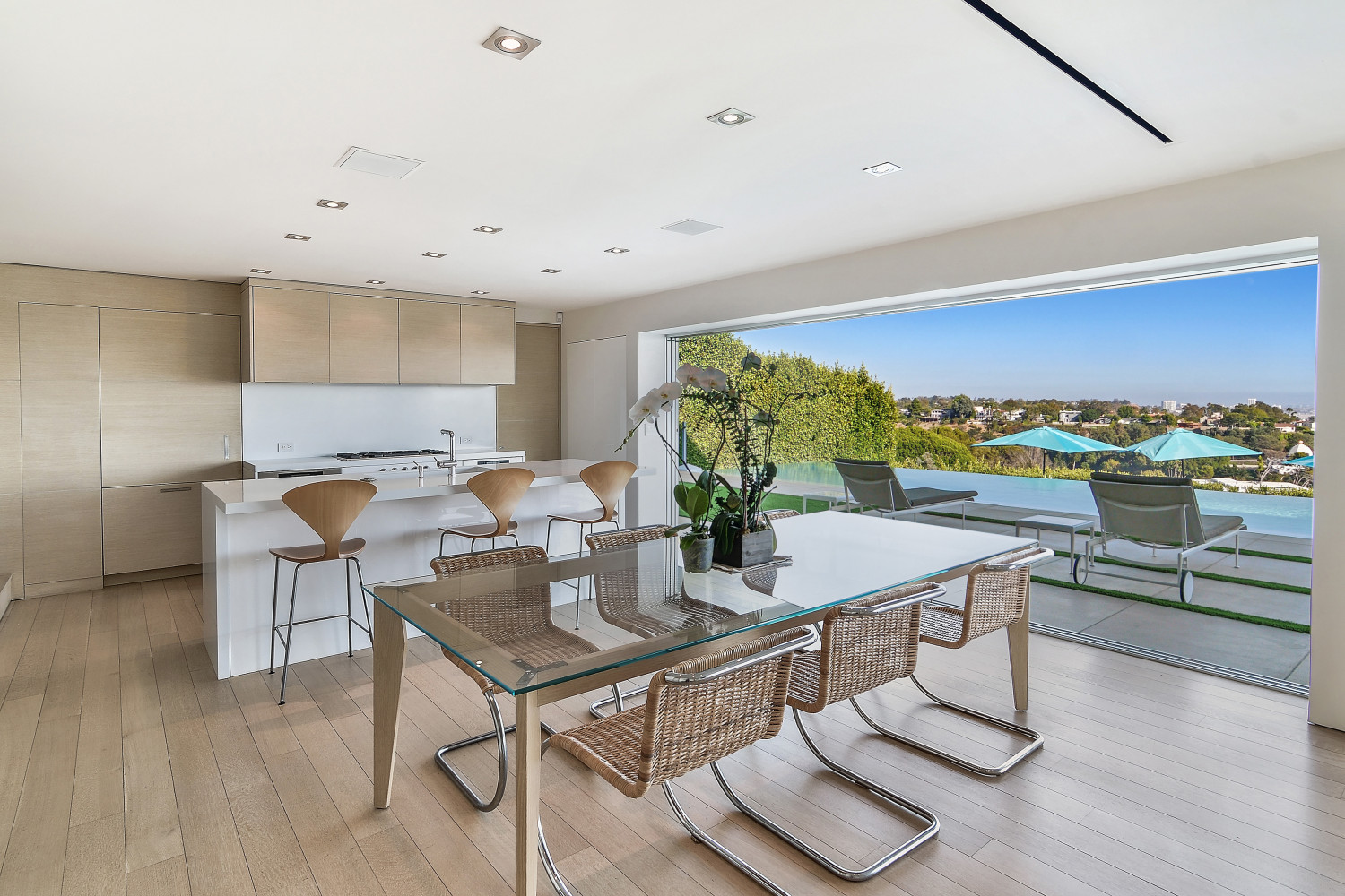 Open-concept kitchen and dining room with floor-to-ceiling glass doors overlooking the infinity pool and Pacific Ocean.